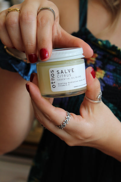 A person with red fingernails removing a the lid of a citrus salve. 