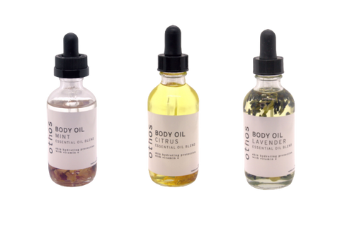Three body oils: from left to right, mint, citrus, and lavender. Bottles have an eyedropper and are made of clear glass.