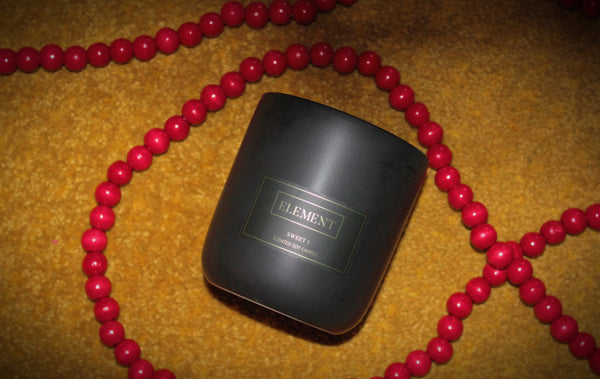 A Sweet One candle laying on a shag yellow surface with red wooden beads draped across.