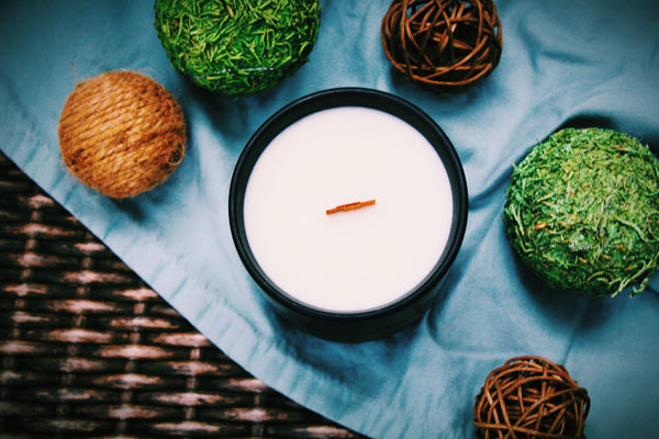 A top view of the candle. Candle is sitting on a blue fabric that is laying across a wicker texture. Surrounding the candle are balls of twine and moss.