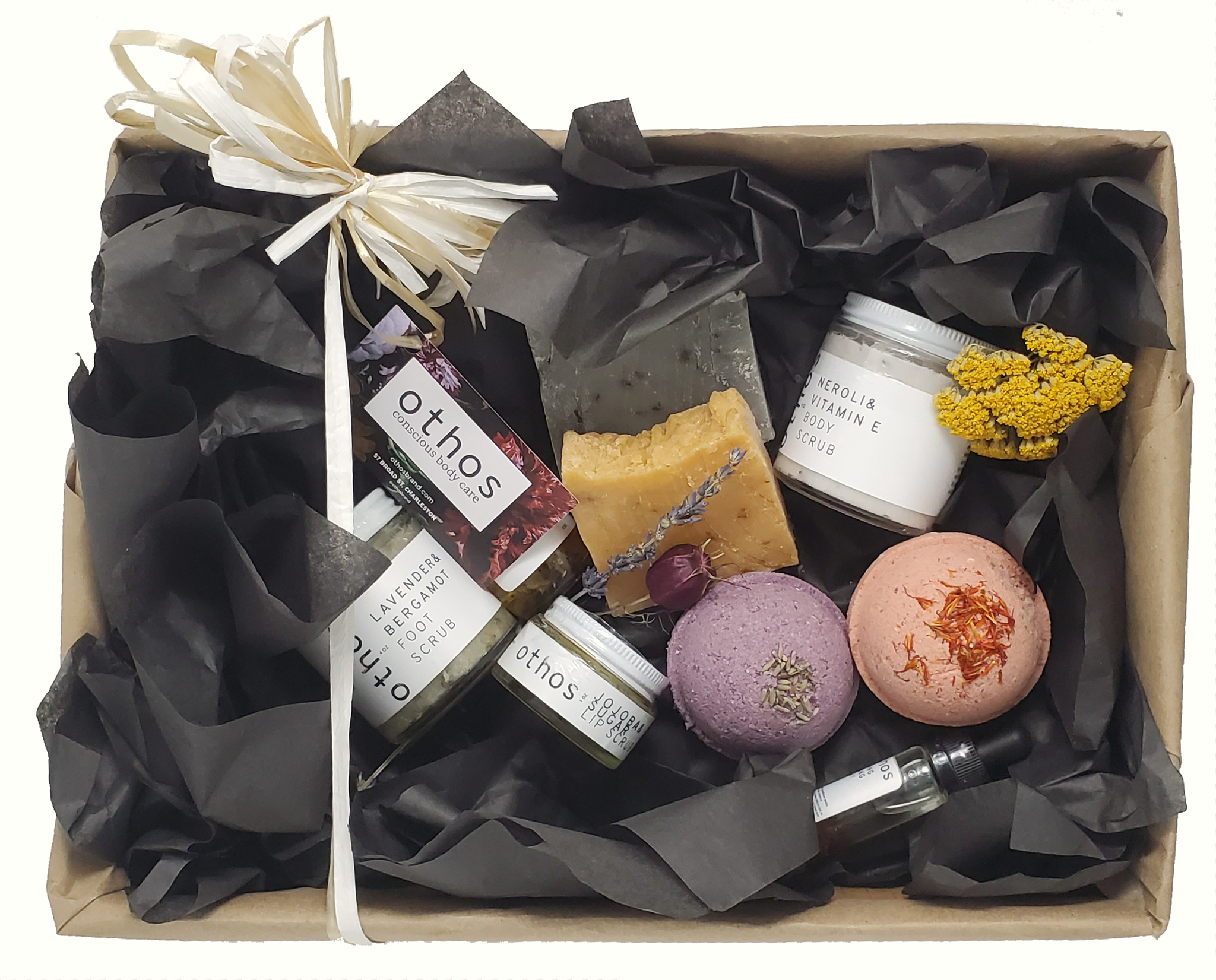 an open gift box of assorted othos products, including two bath bombs (lavender and ylang ylang), two bars of soap (citrus and mint), and lip scrub, body scrub, foot scrub, and body oil.